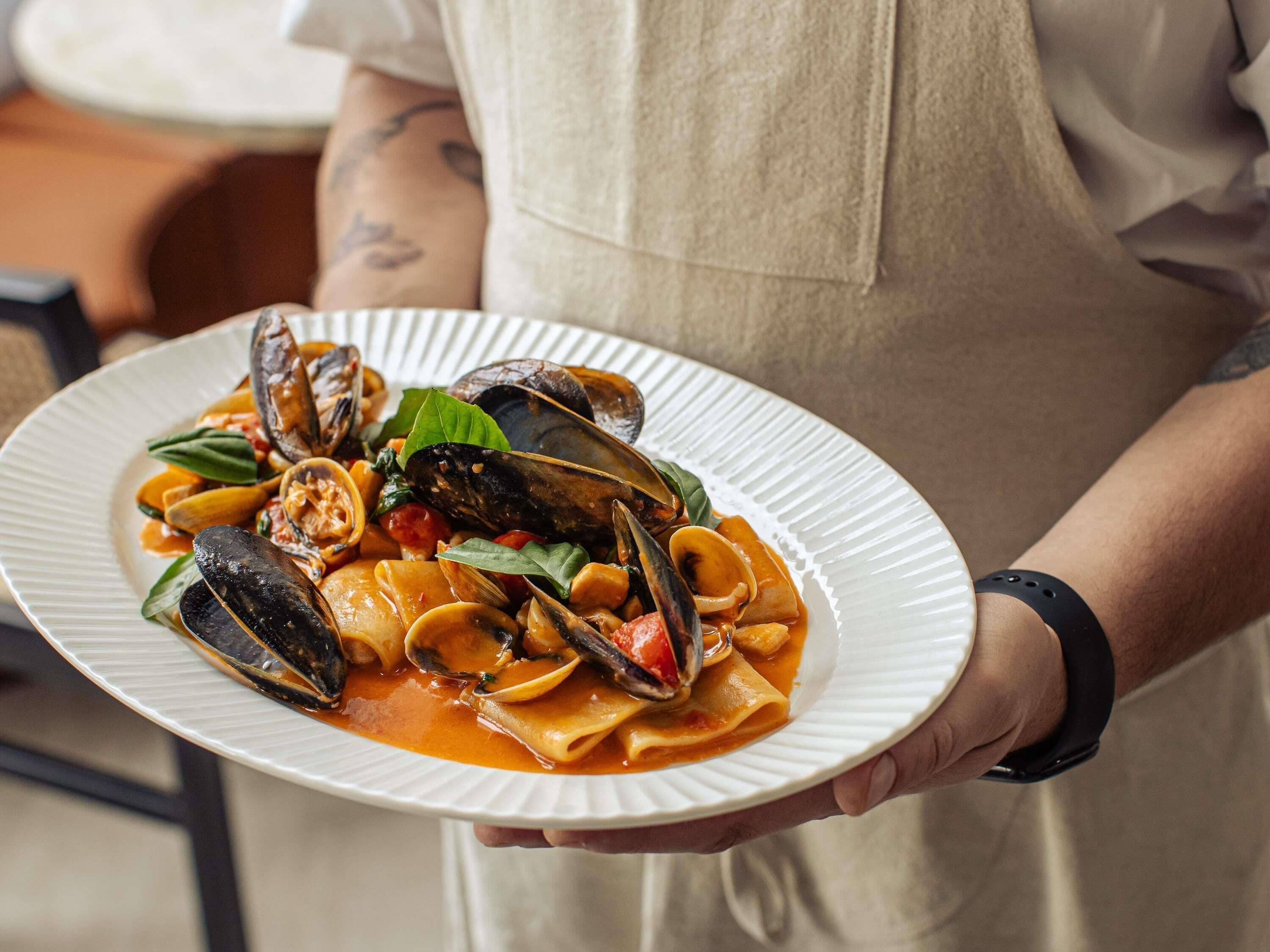 A person holding a plate of pasta with mussels and vegetables.
