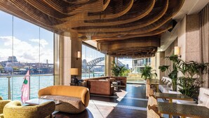 A spacious lounge with a view of the Sydney Harbour Bridge, featuring comfortable seating, a reception area, and a large window overlooking the water.
