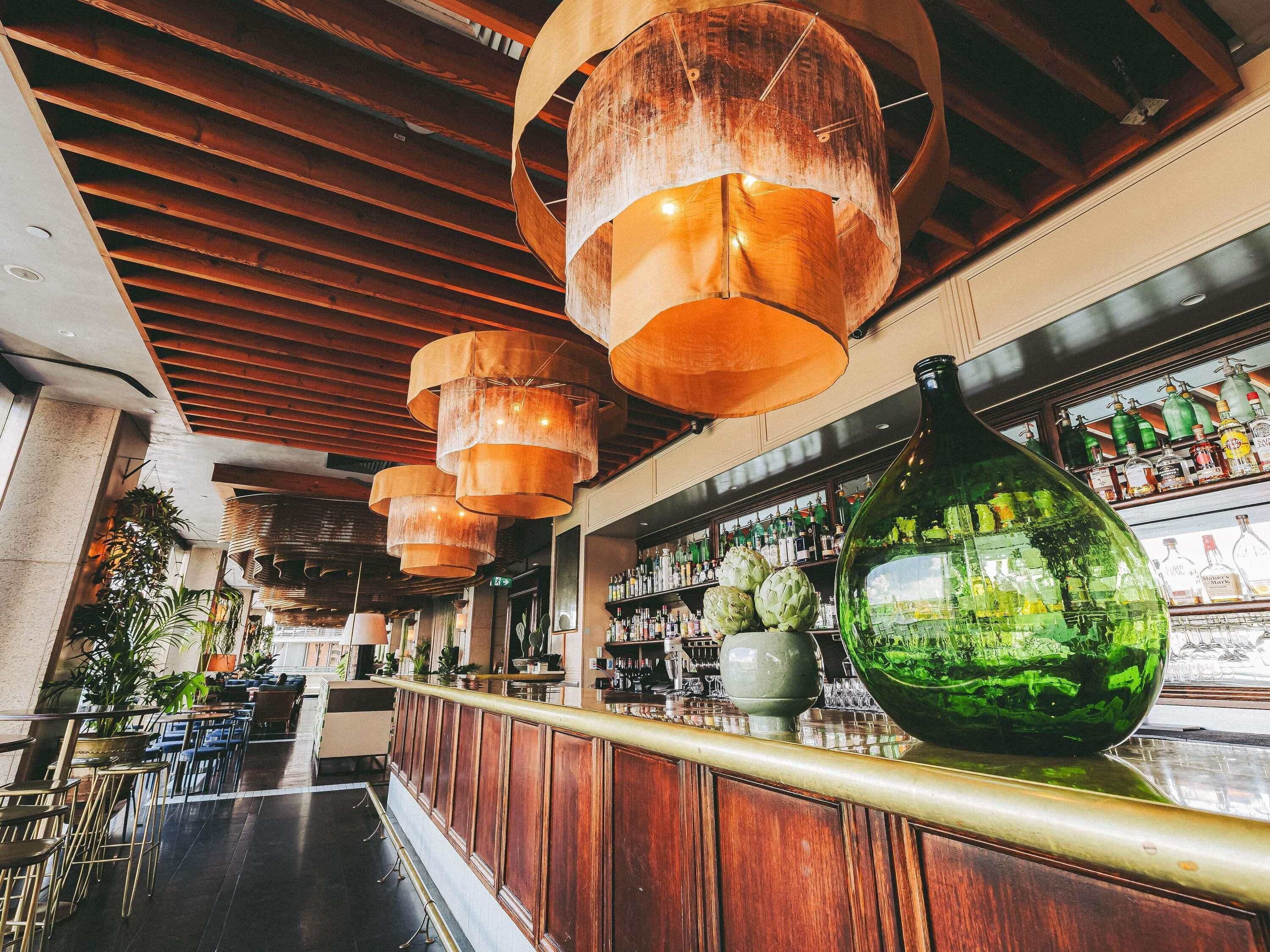 A bar area with wooden ceiling beams, hanging lamps, and a large green vase on the counter.