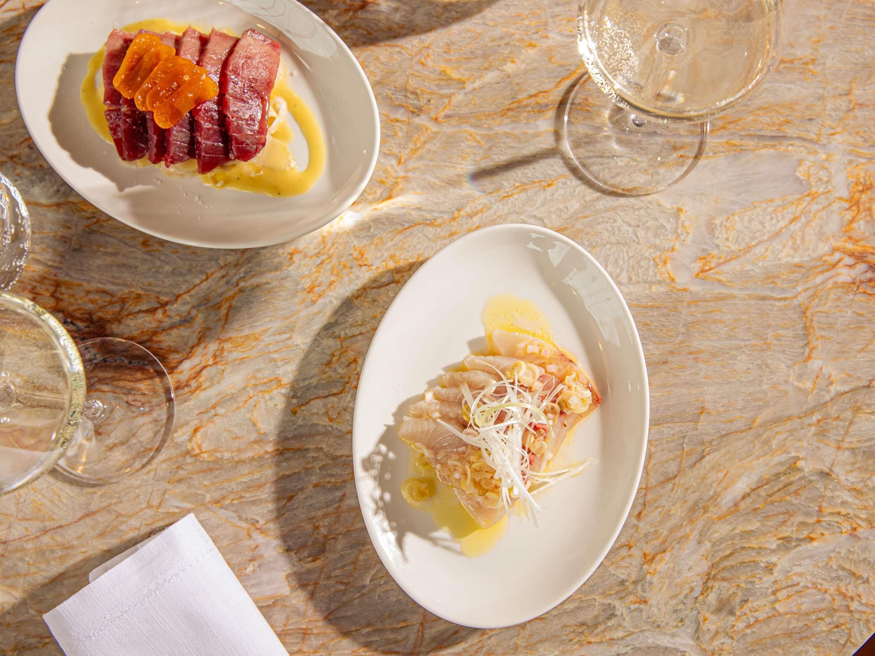 A marble table with two plates of food and two glasses of white wine.