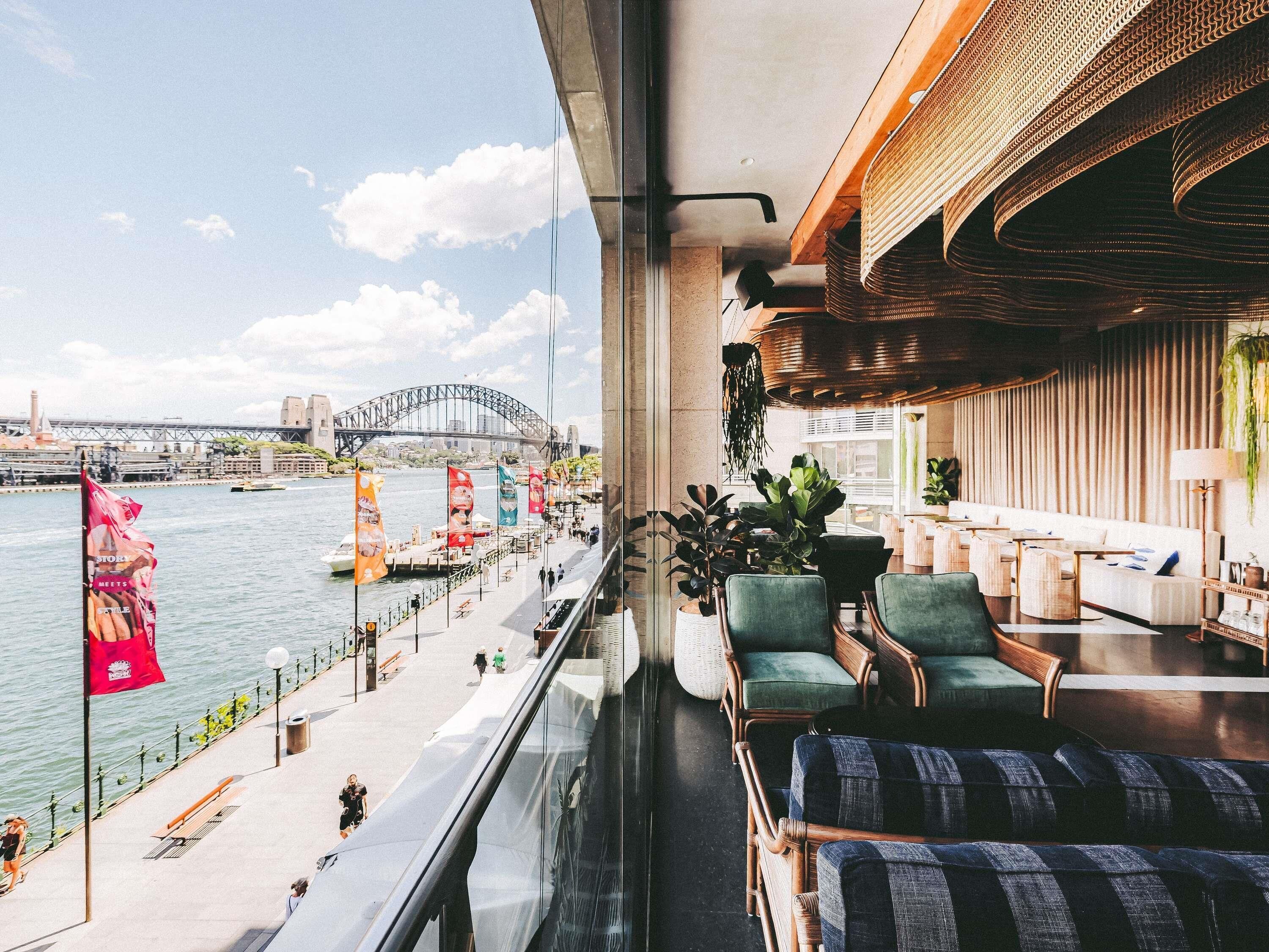 A balcony with a view of the Sydney Harbour Bridge, seating area with wicker chairs, and a modern interior design.