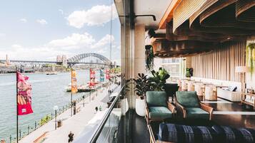 A balcony with a view of the Sydney Harbour Bridge, seating area with wicker chairs, and a modern interior design.