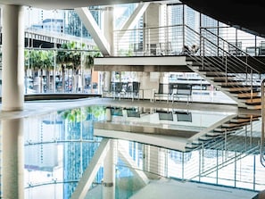 Un espacio interior moderno con piso reflectante, zonas de estar y una escalera que conduce a un nivel superior.