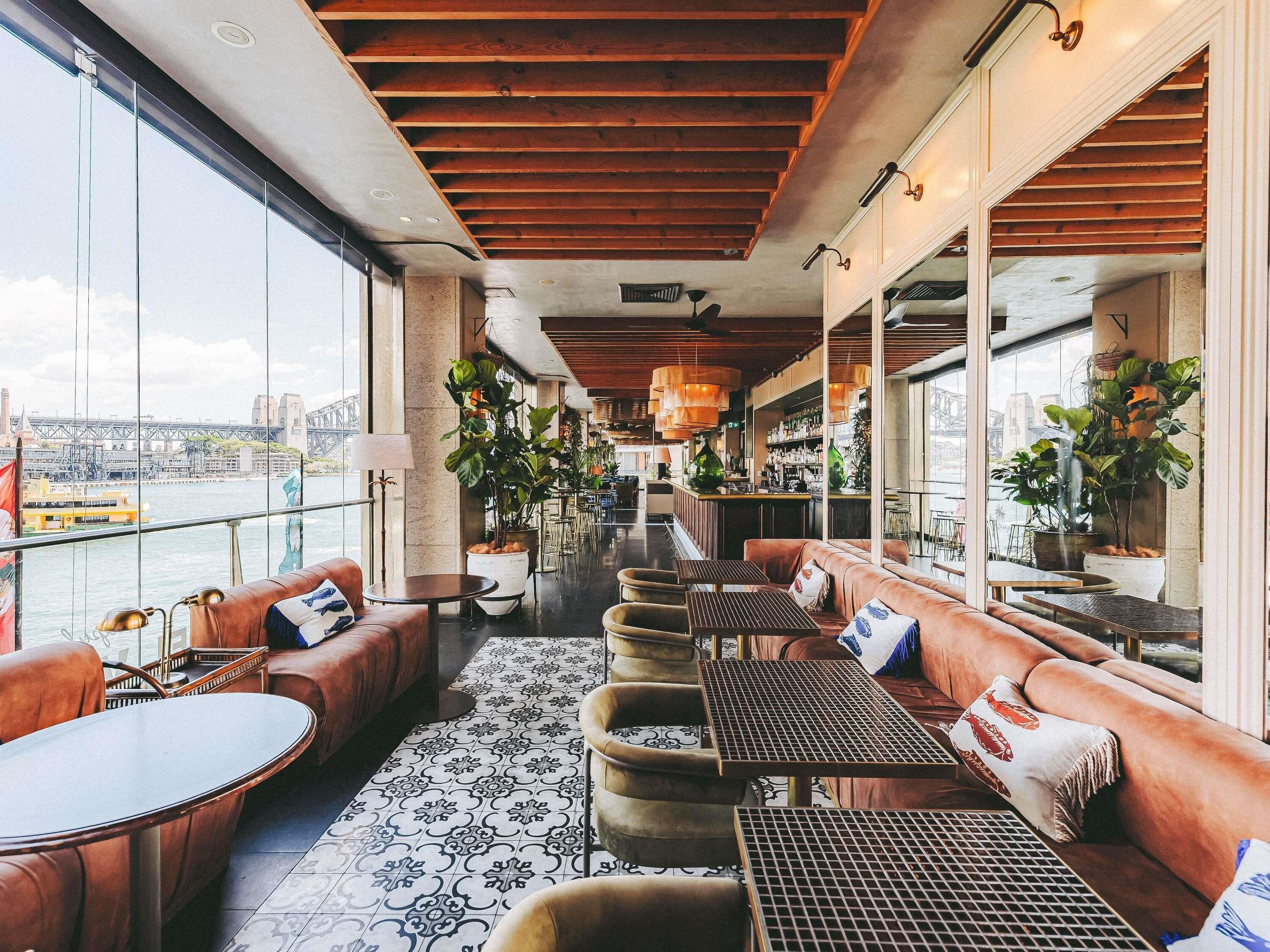 Um espaço amplo e interno com assentos, um bar e janelas grandes que oferecem vista para a cidade.