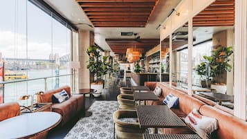 Amplio espacio interior con arreglos de asientos, un bar y grandes ventanales con vista a la ciudad.