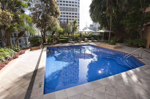 Una piscina interior con suelo de baldosas, rodeada de vegetación y sillones de descanso.