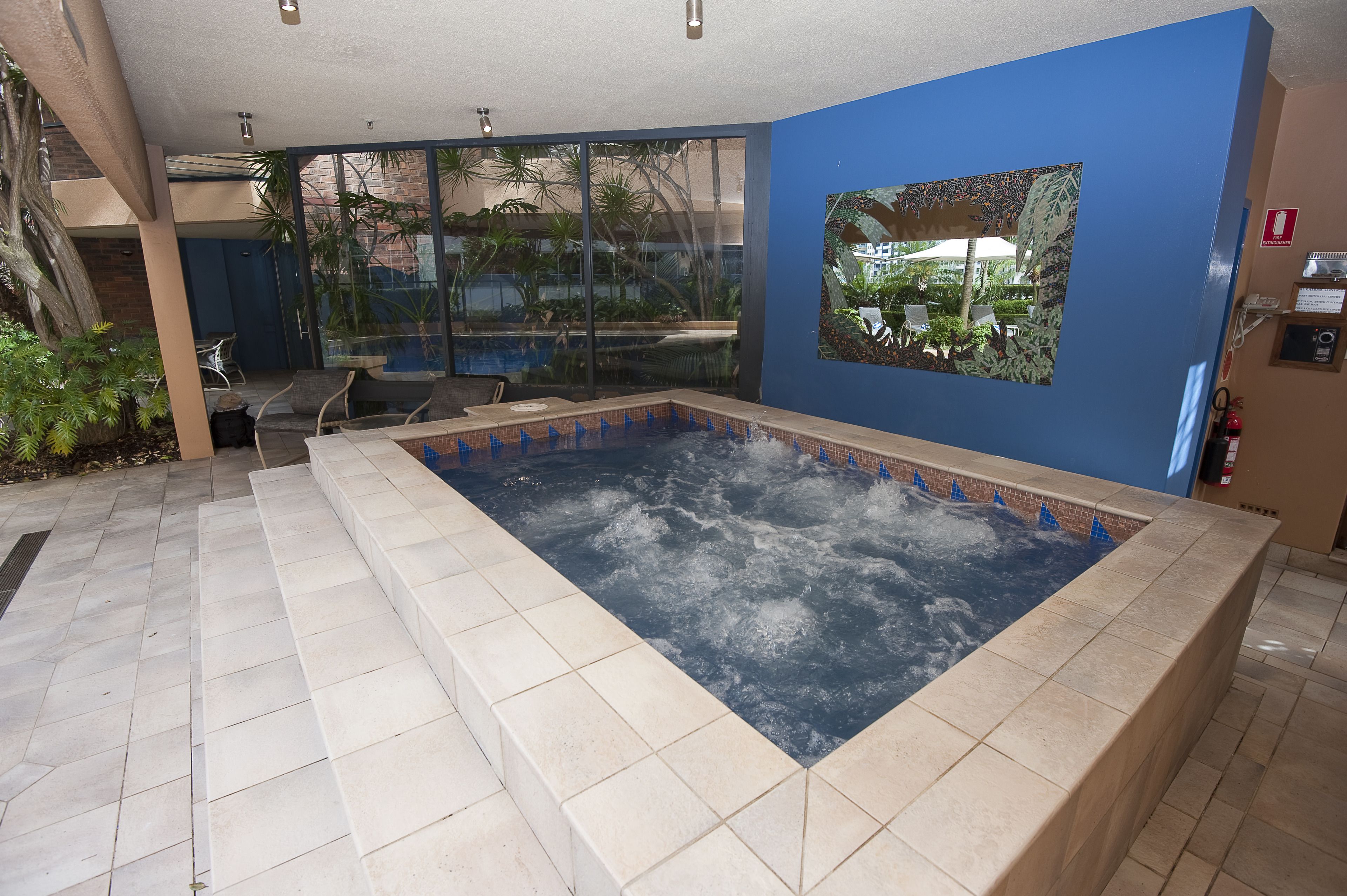 Ein Wellnessbereich mit Whirlpool, einer Glaswand mit Blick ins Freie und einer blauen Wand mit einem gerahmten Bild.