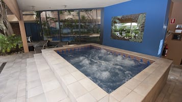 Un área de spa con hidromasaje, un muro de cristal con vistas al exterior y una pared azul con un cuadro enmarcado.