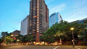 Un edificio de gran altura con varios pisos y un diseño arquitectónico moderno, rodeado de árboles y farolas.