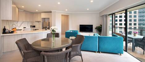 Un apartamento moderno con cocina, comedor y sala de estar. Cuenta con un ventanal grande, televisor de pantalla plana y balcón con vistas a la ciudad.