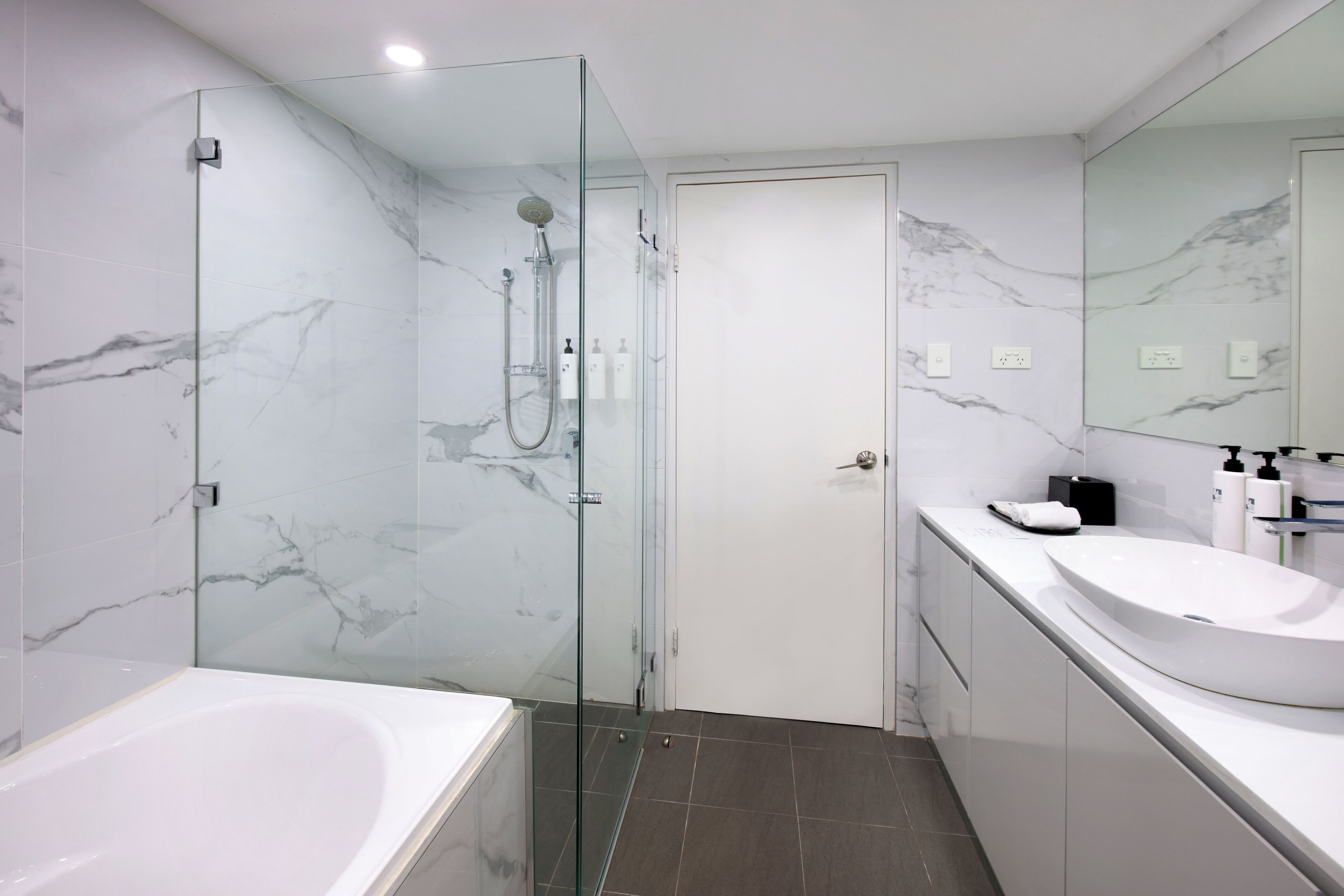 A modern bathroom with a glass-enclosed shower, a white bathtub, and a large sink.