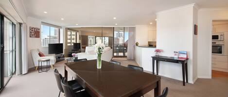 A modern living room with a dining table, black chairs, a sofa, and a TV.