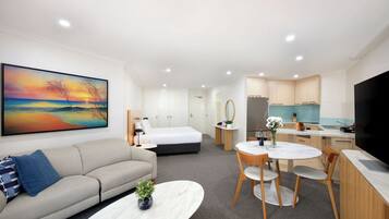 Une chambre d’hôtel moderne comprenant un lit, un canapé, un coin repas avec une table et des chaises, un coin cuisine avec un réfrigérateur et un téléviseur.