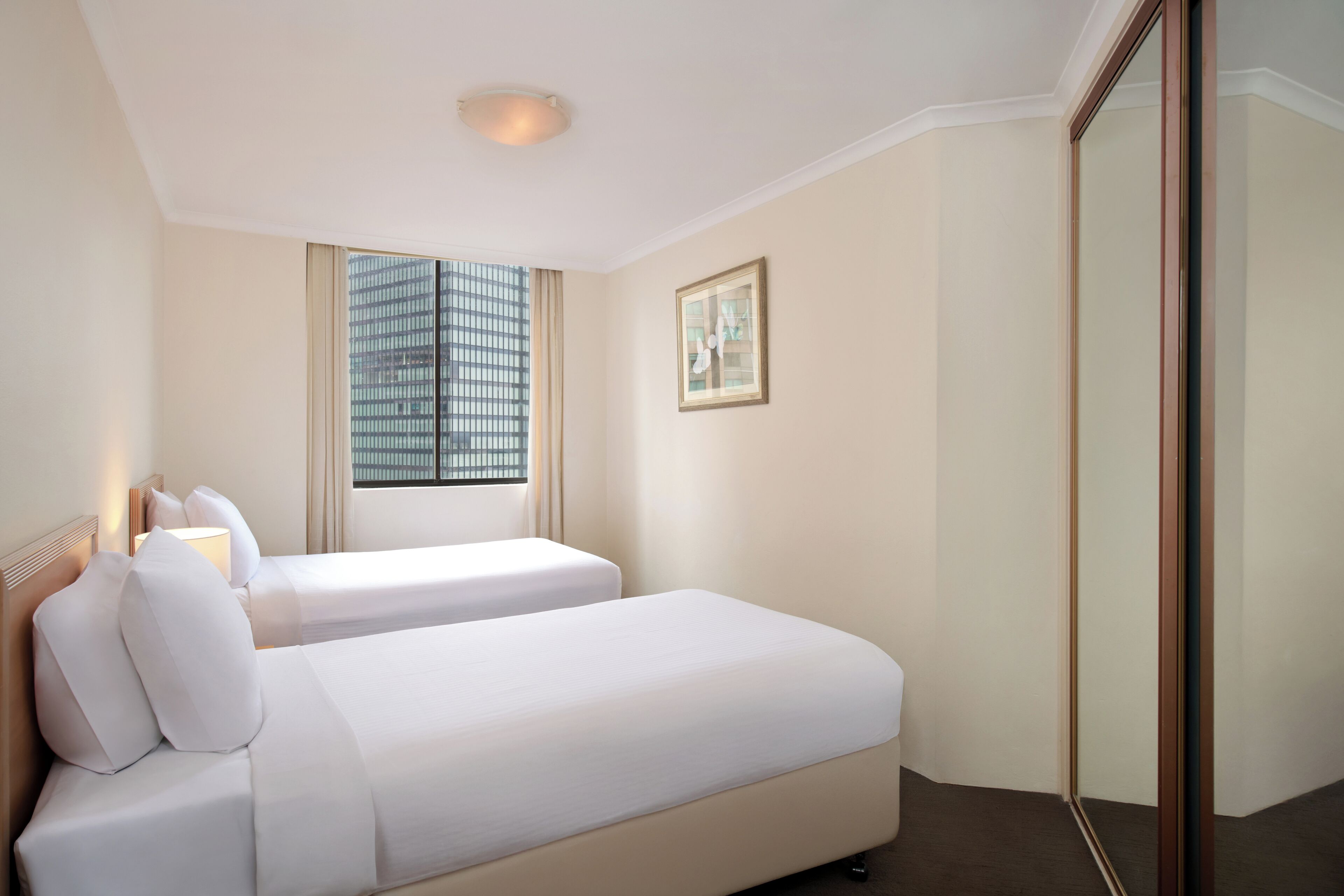Habitación de hotel con dos camas, un ventanal con persianas, un cuadro en la pared y un espejo.