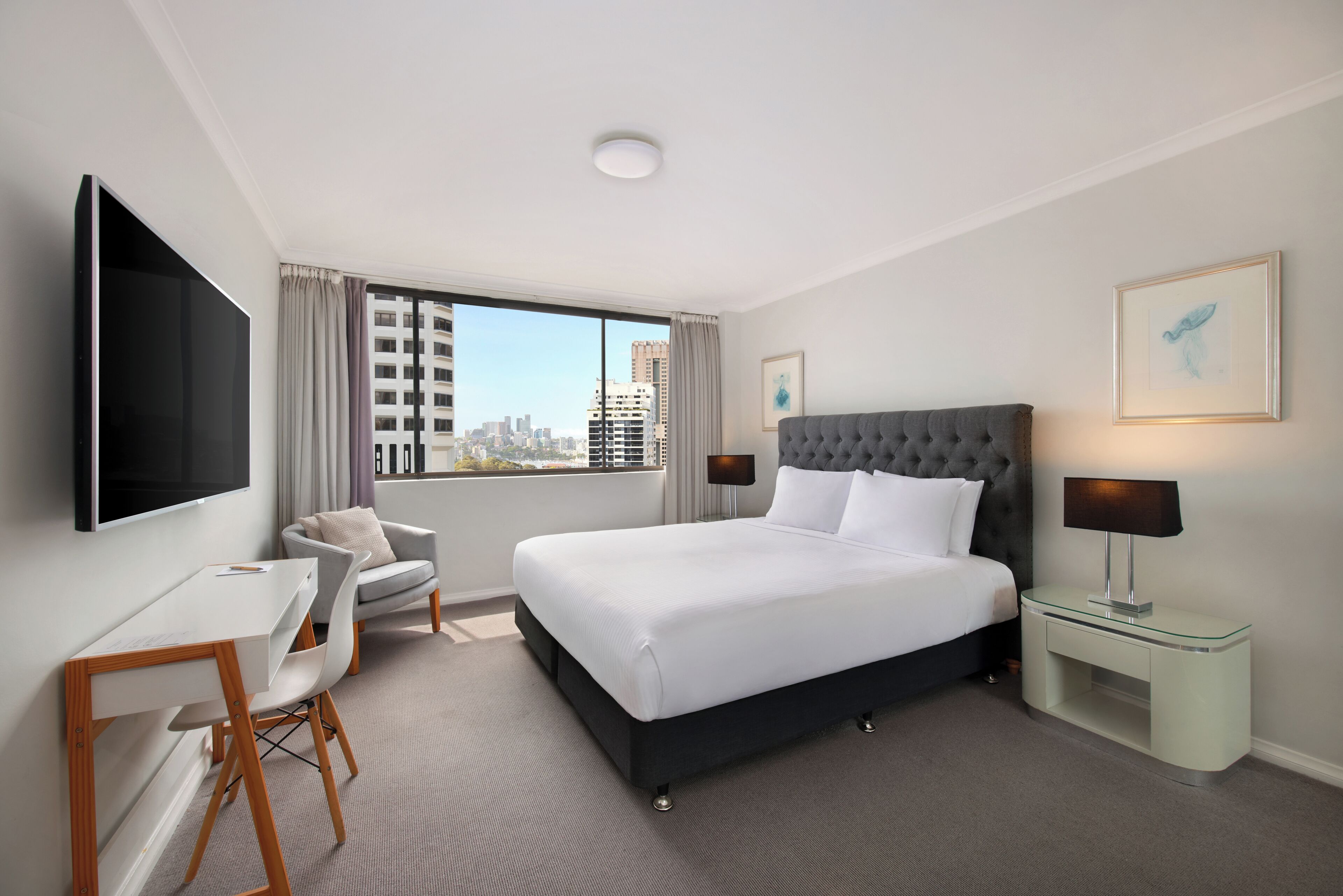 Une chambre d’hôtel avec un grand lit, un bureau, une chaise, une télévision et une fenêtre donnant sur la ville.