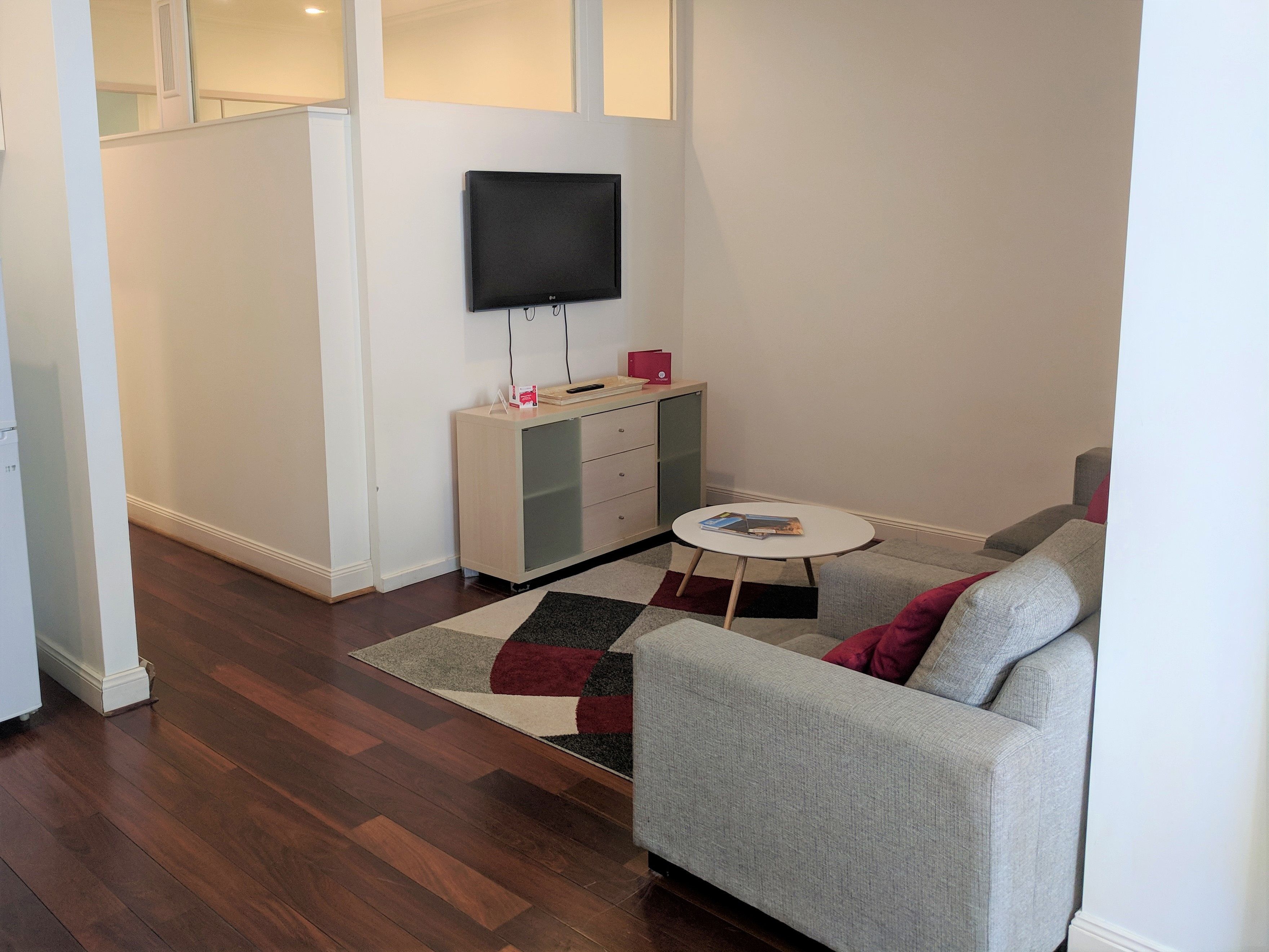 A modern living room with a grey sofa, a small white coffee table, and a flat-screen TV mounted on the wall.