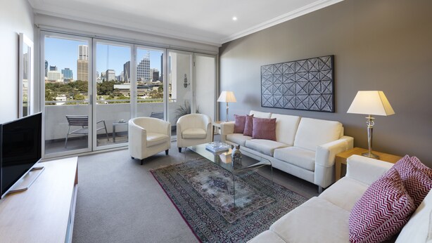 Un salon moderne avec vue sur la ville, des meubles blancs et une table basse en verre.