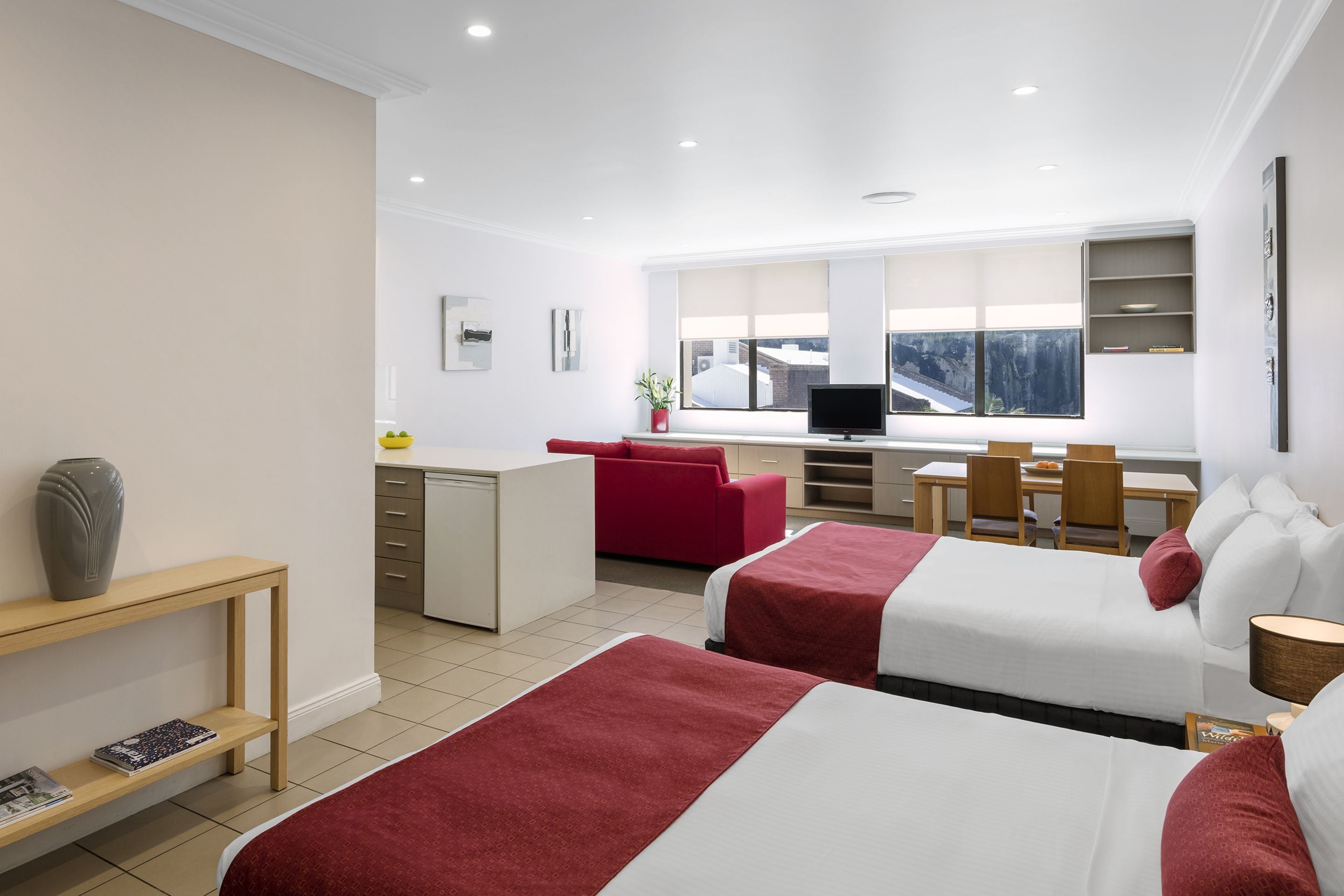 Habitación de hotel con dos camas, un escritorio, un sofá rojo, un televisor y una ventana con vistas.