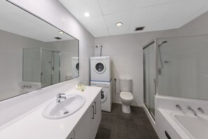 Et moderne badeværelse med et stort spejl, vask, vaskemaskine, toilet og bruser.