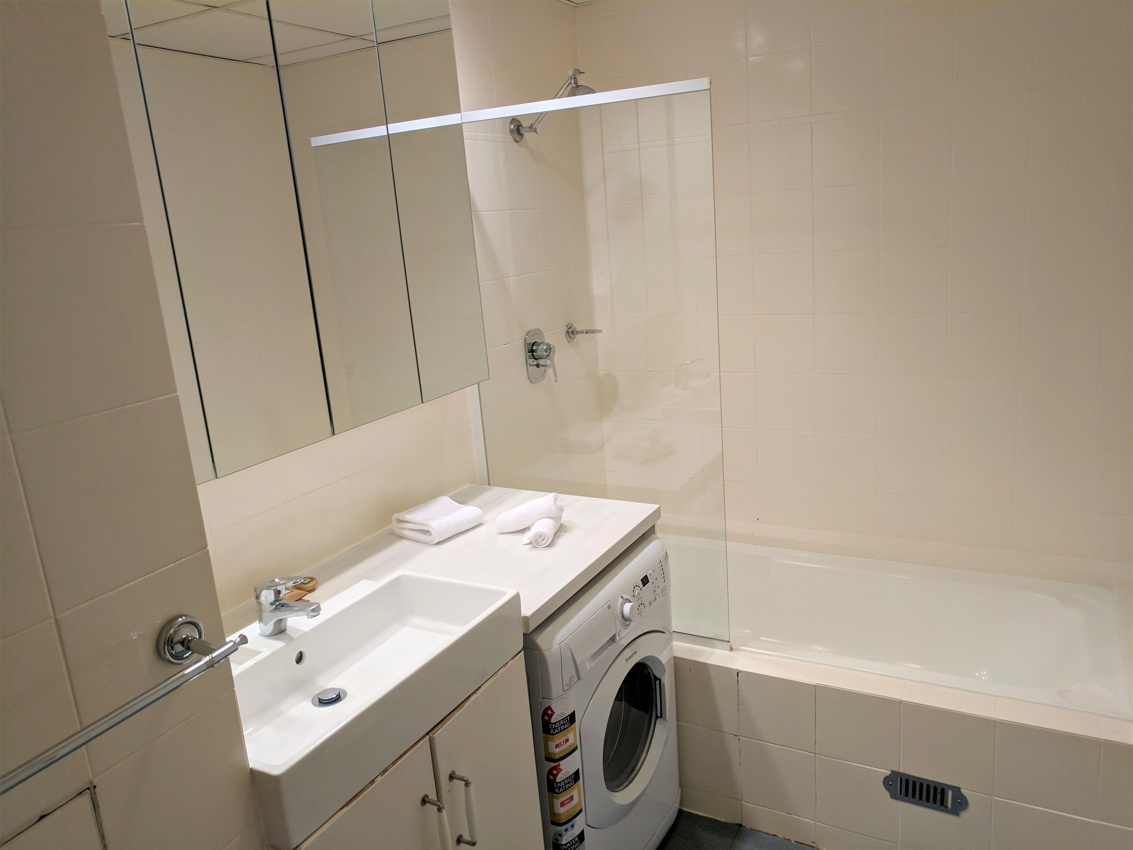 Une salle de bain équipée d’un lavabo, d’un miroir, d’un porte-serviettes et d’un lave-linge.