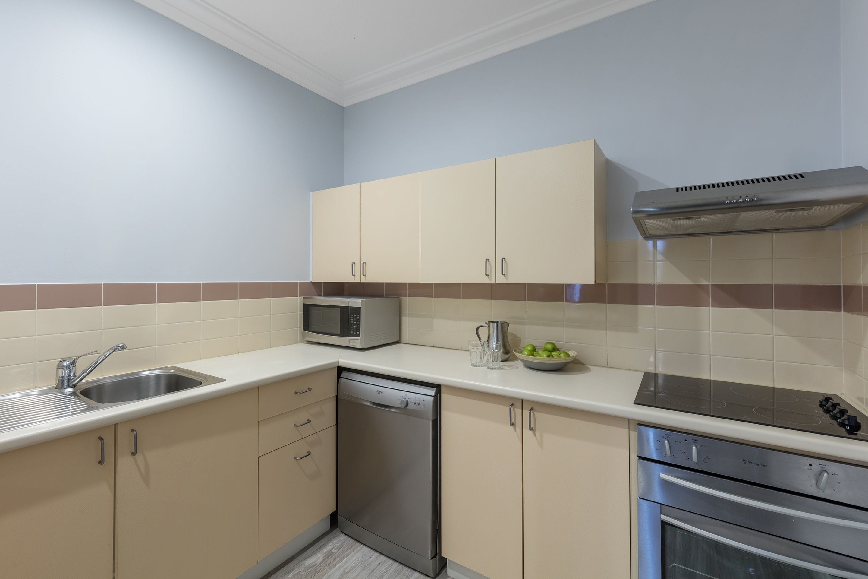 A kitchen with beige cabinets, a stainless steel dishwasher, a microwave, a gas stove, and a stainless steel oven.