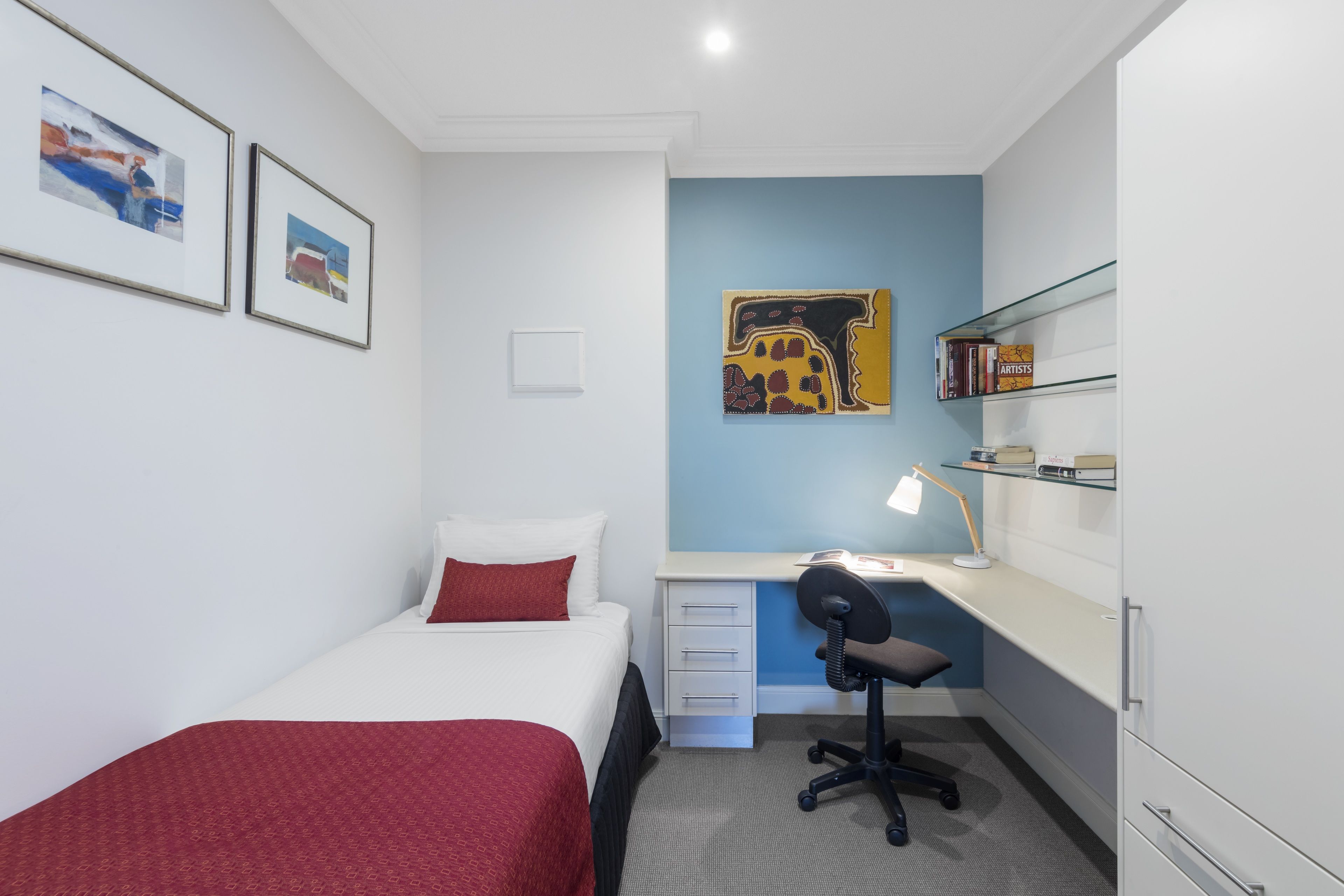 A bedroom with a bed, desk, chair, and a shelf with books.