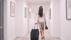 Un couloir avec des œuvres d’art encadrées accrochées aux murs, une personne qui marche avec une valise et une porte sur la gauche.