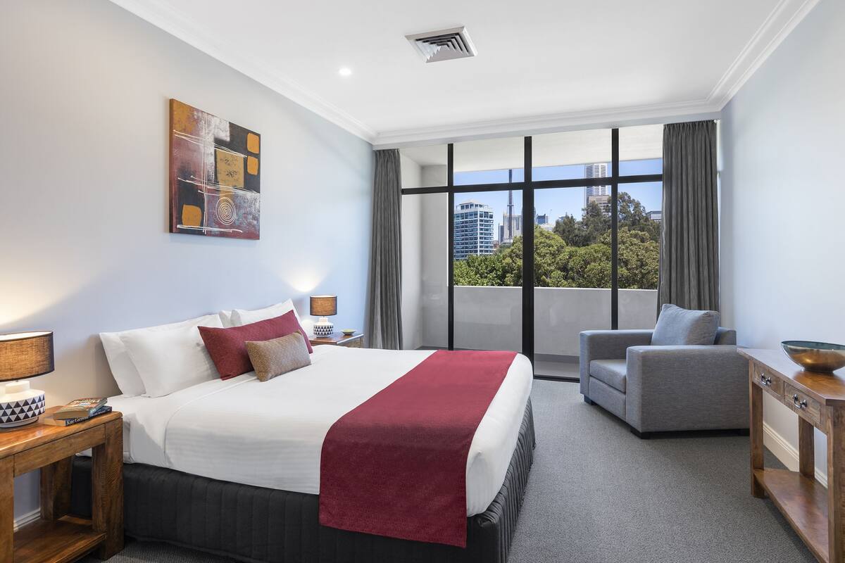 Habitación de hotel moderna con una cama grande, un sofá gris y vistas a la ciudad.