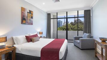 A modern hotel room with a large bed, a grey sofa, and a view of the city.