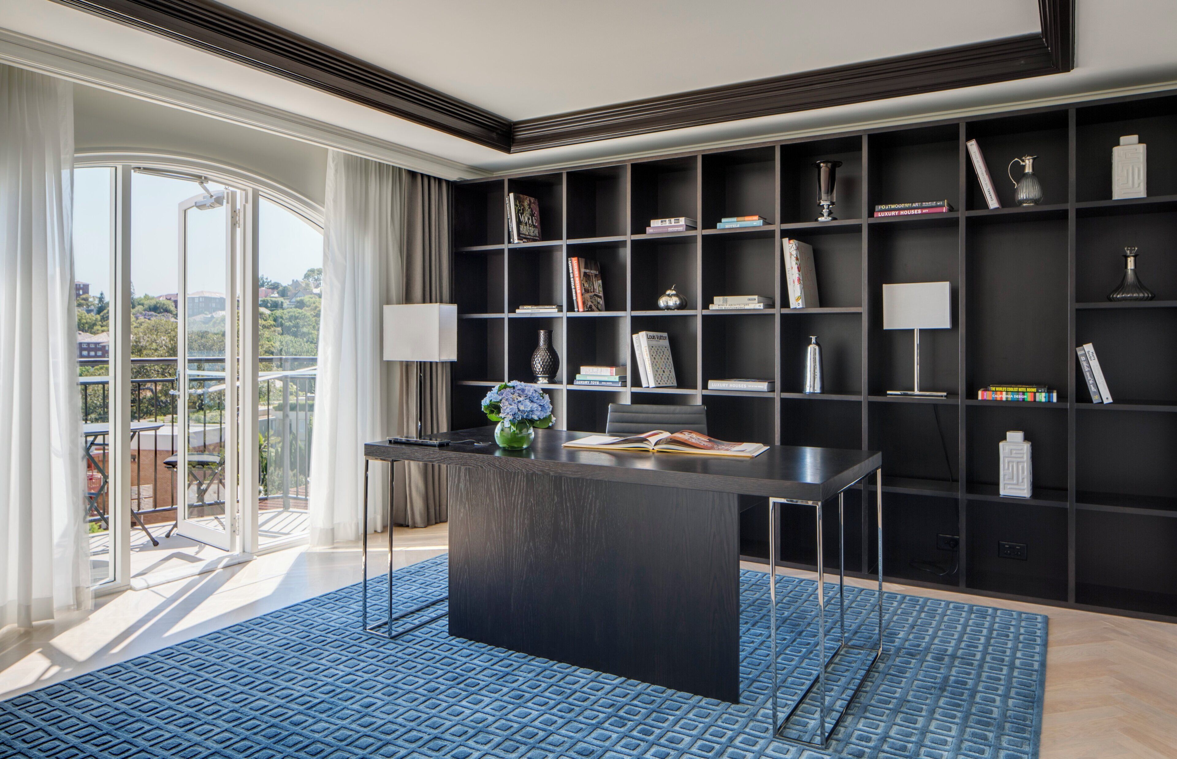 A modern interior with a dark wood desk, a bookshelf, and a view through a glass door.