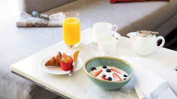 A breakfast setup on a table with croissants, a bowl of yogurt with berries, a glass of orange juice, and a coffee pot.