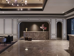 A lobby with a marble reception desk, a chandelier, and a vase with flowers.