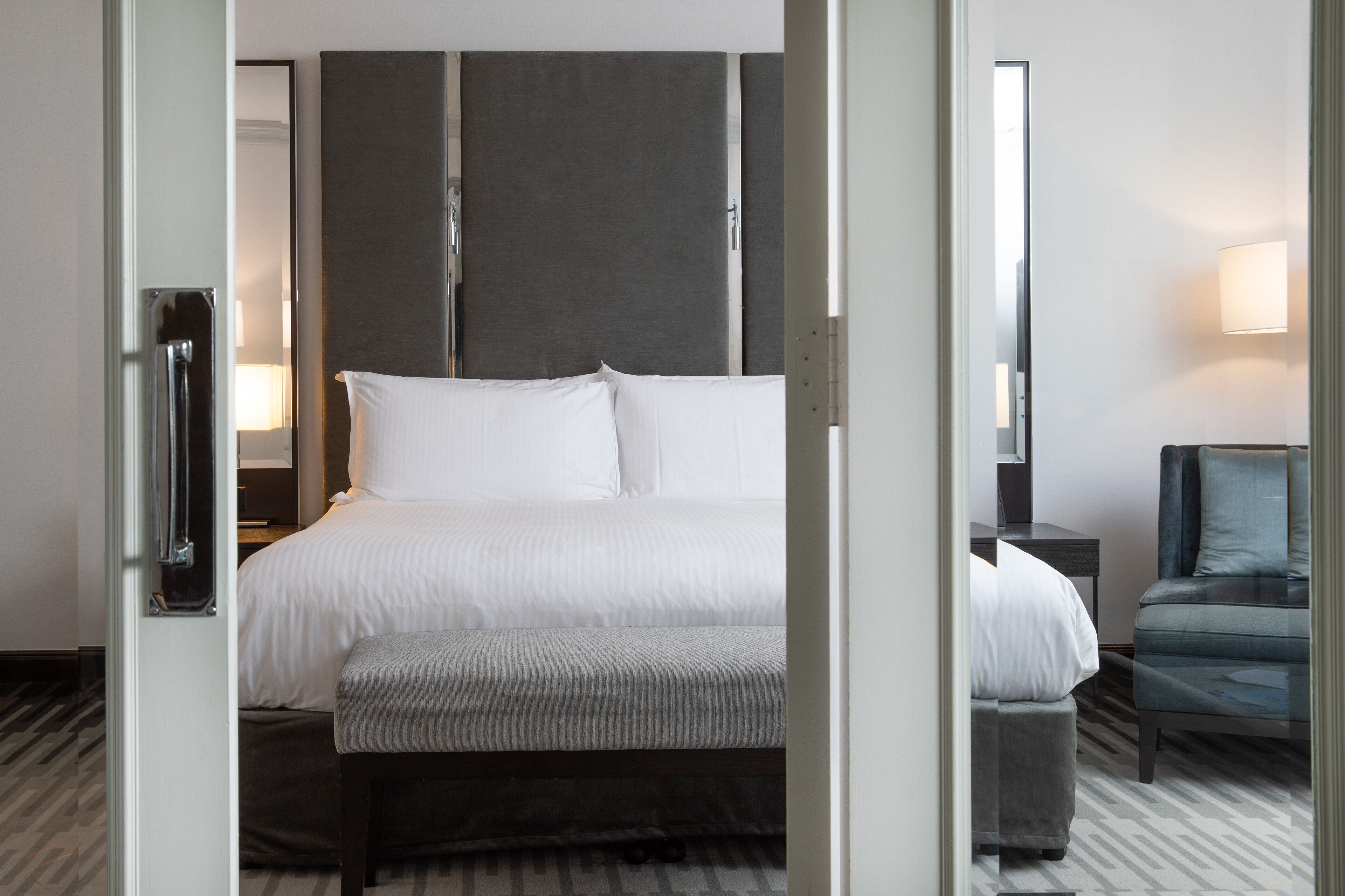 A hotel room with a bed, a chair, a nightstand, and a lamp.