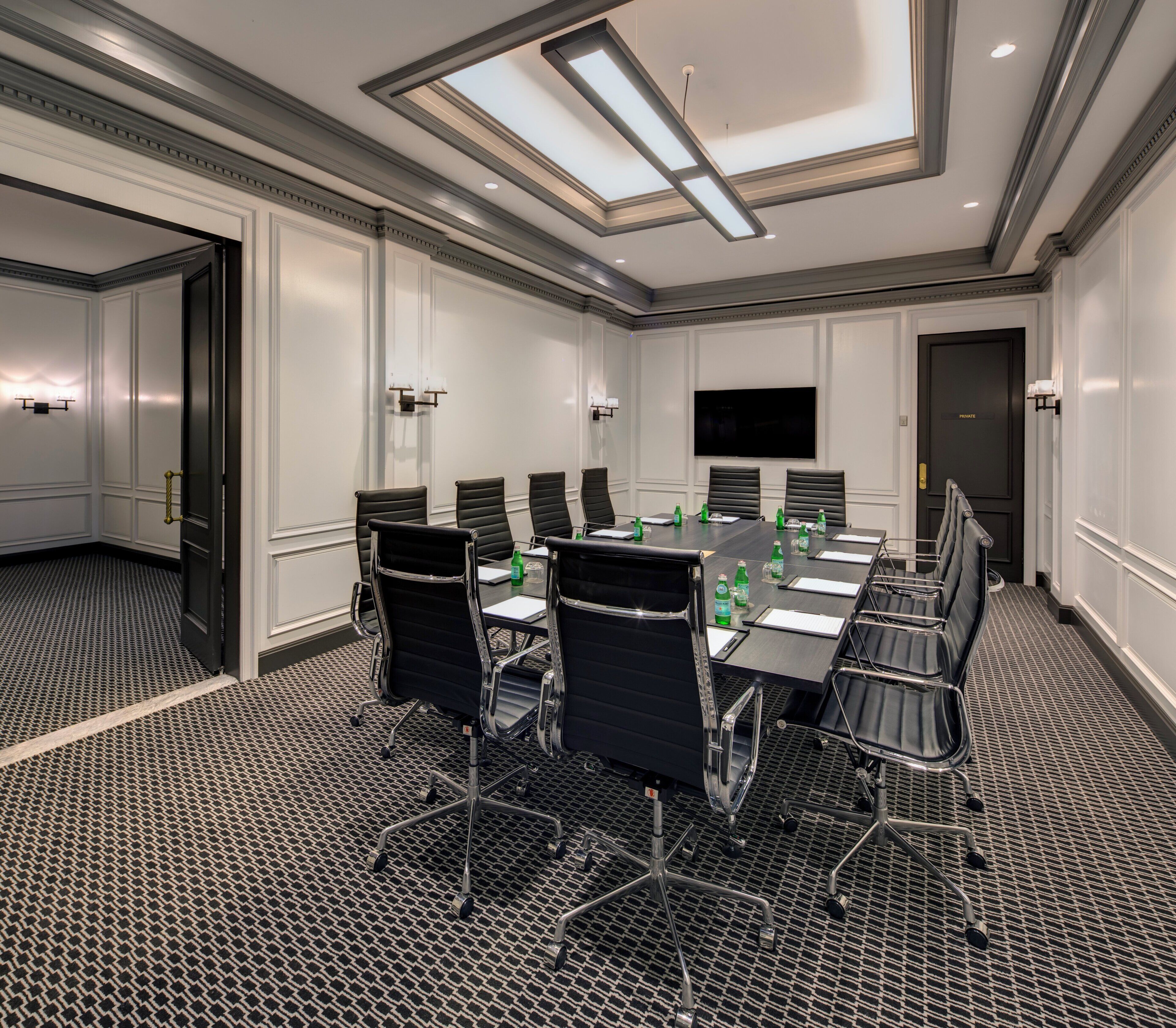 A conference room with a long table, multiple chairs, a flat-screen TV, and a patterned carpet.