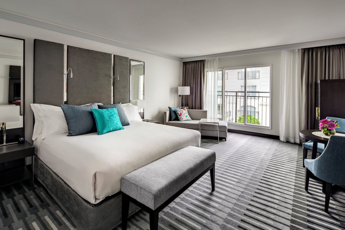 A hotel room with a large bed, a seating area with a table, and a view of the city.