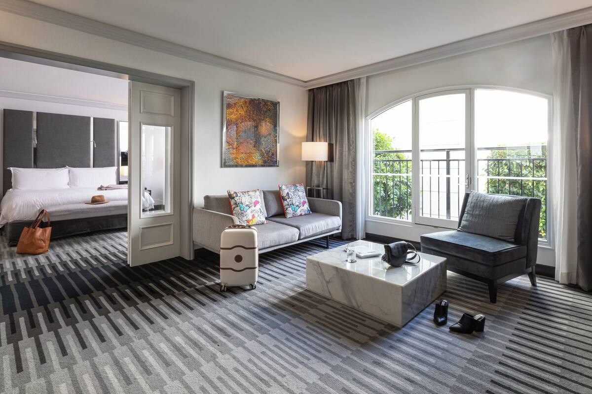 A hotel room with a bed, a sofa, a coffee table, and a view of the outdoors.