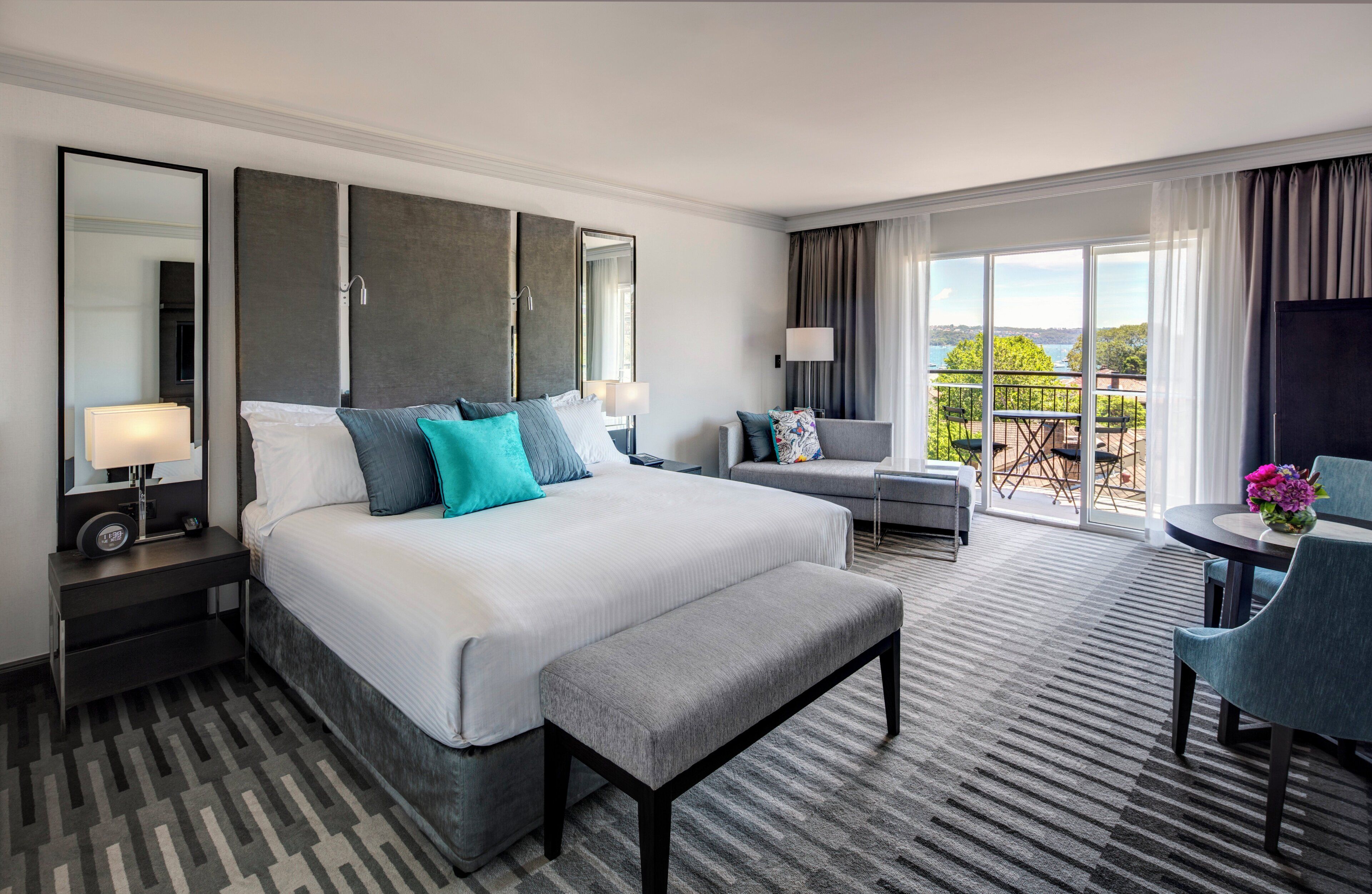 A hotel room with a large bed, a desk, a chair, and a balcony with a view.