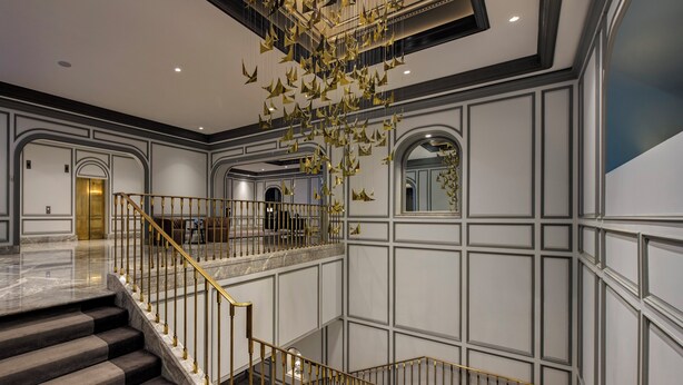 Un interior imponente con una escalera de mármol, un candelabro y un techo alto.