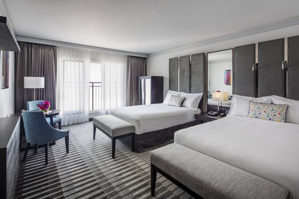 A hotel room with two beds, a desk, a chair, and a large window with curtains.