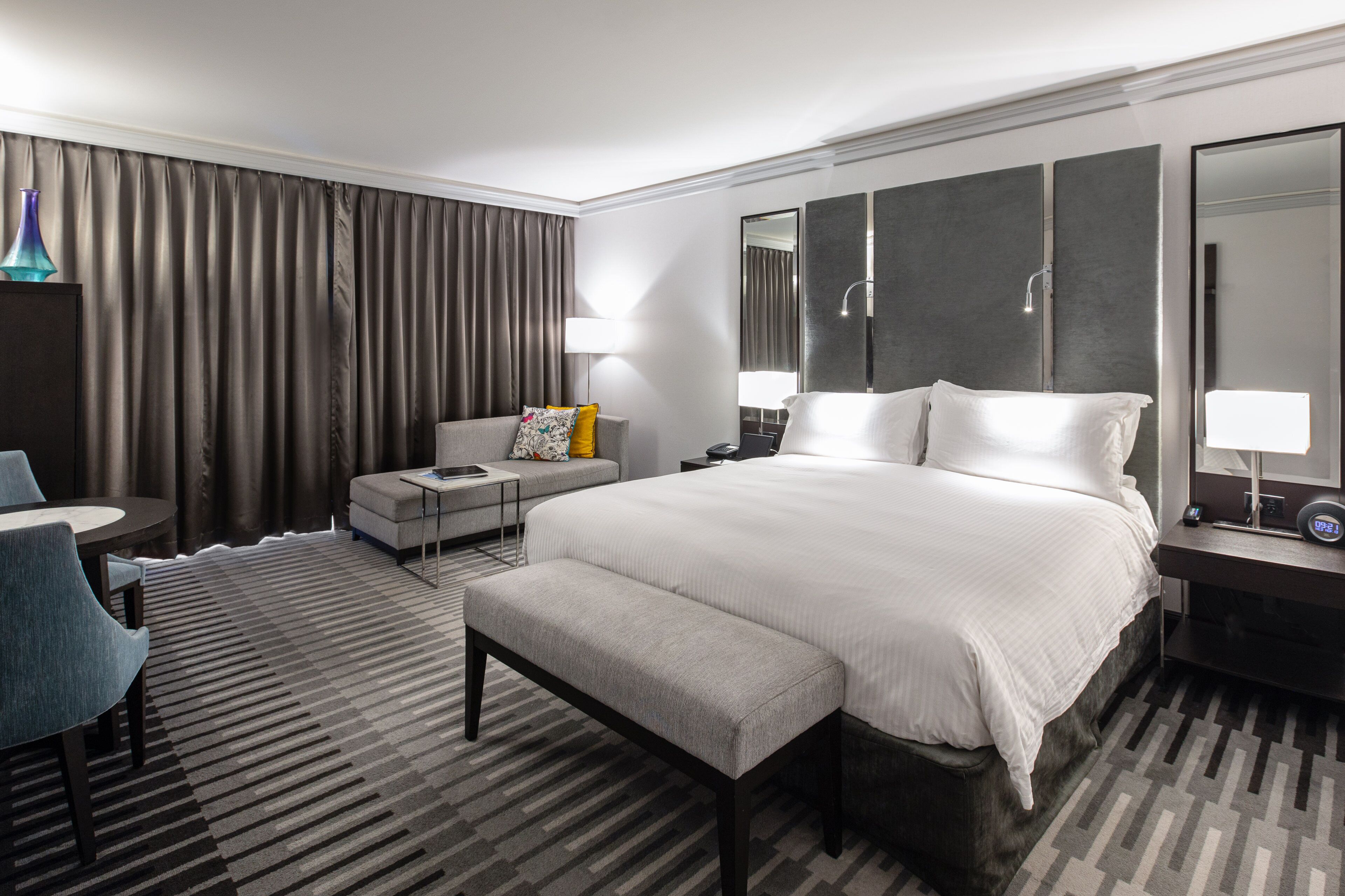 Habitación de hotel con una cama grande, escritorio, silla, sofá y baño con espejo y ducha.