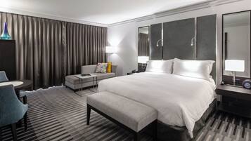Habitación de hotel con una cama grande, escritorio, silla, sofá y baño con espejo y ducha.