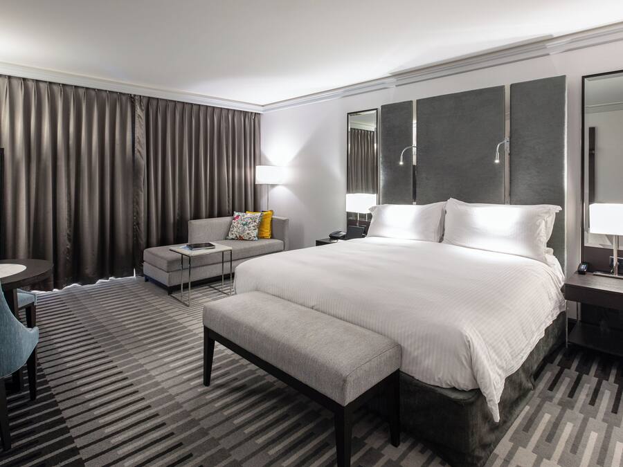Habitación de hotel con una cama grande, escritorio, silla, sofá y baño con espejo y ducha.