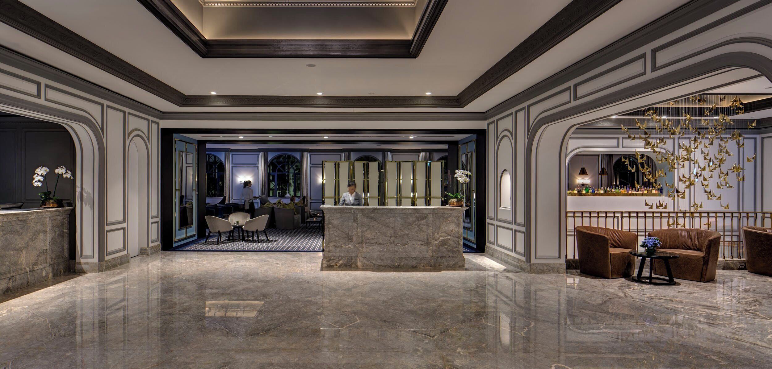 A lobby with a marble floor, a reception desk, seating area, and a bar with hanging decorations.