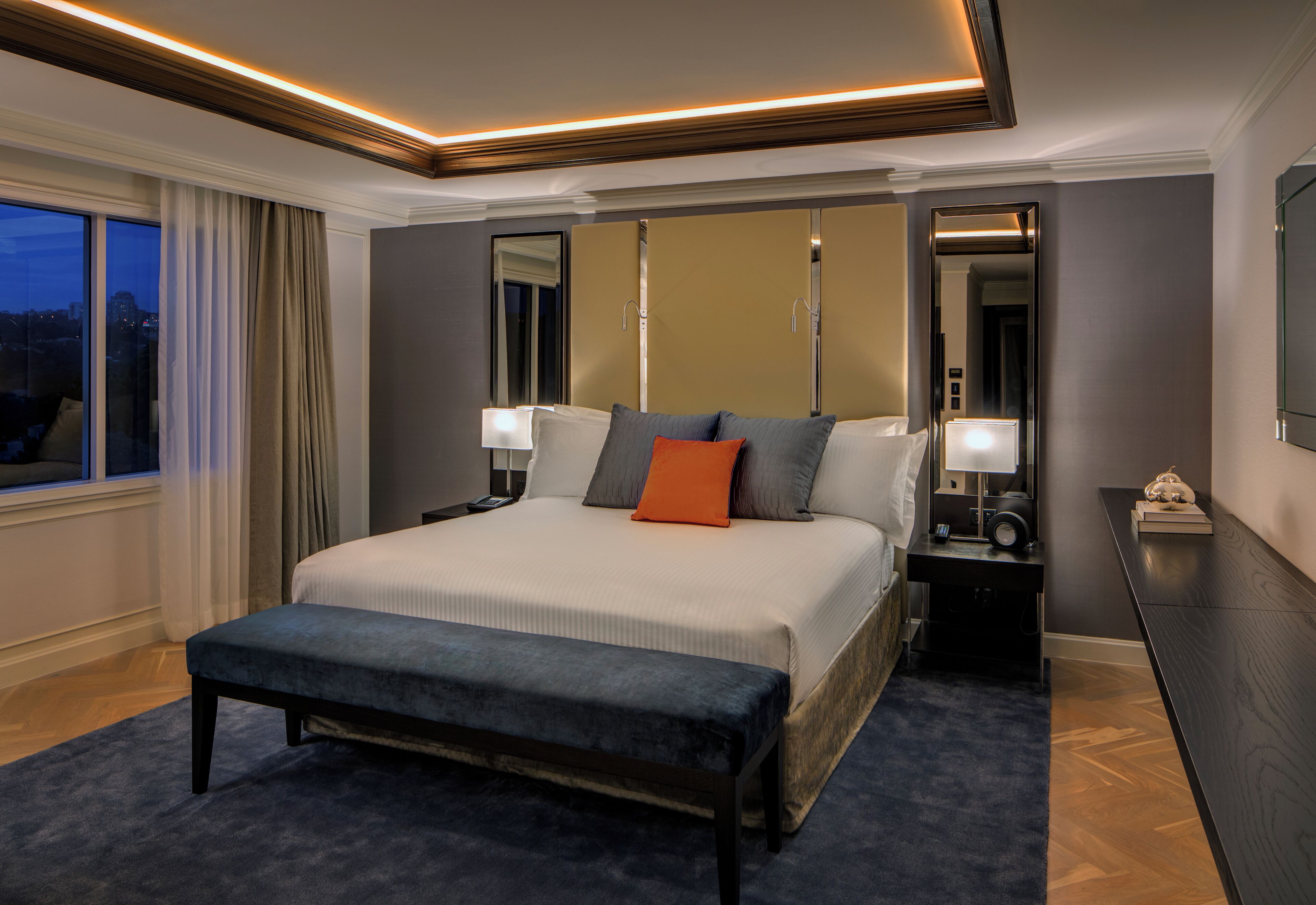 A modern hotel room with a large bed, bedside tables, a desk, and a view of the city.