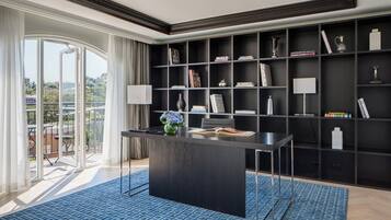 A modern office space with a large desk, bookshelves, and a view of a balcony.