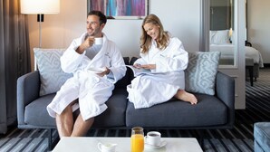 A couple in white robes sitting on a grey sofa in a hotel room with a coffee table, a lamp, and a painting on the wall. - InterContinental Sydney Double Bay by IHG (Double Bay)