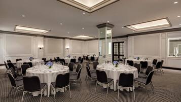 A conference room with multiple round tables, black chairs, and white tablecloths.