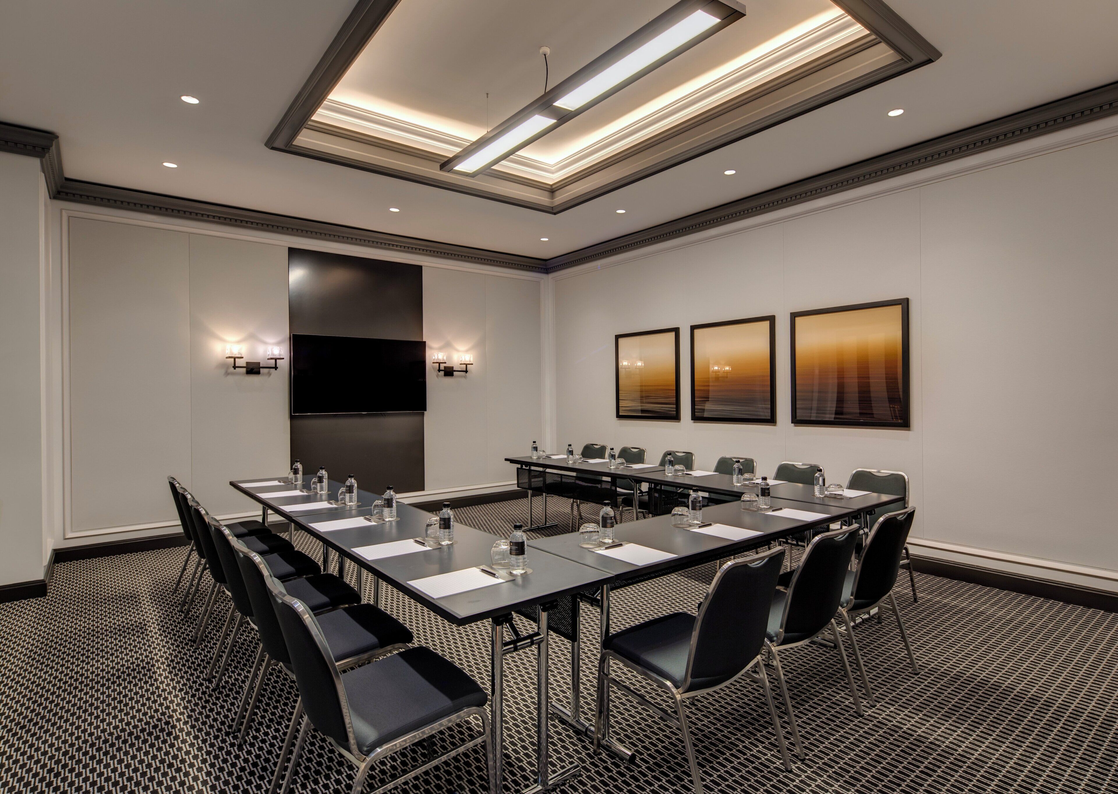 A conference room with a long table, chairs, a flat-screen TV, and three framed pictures on the wall.