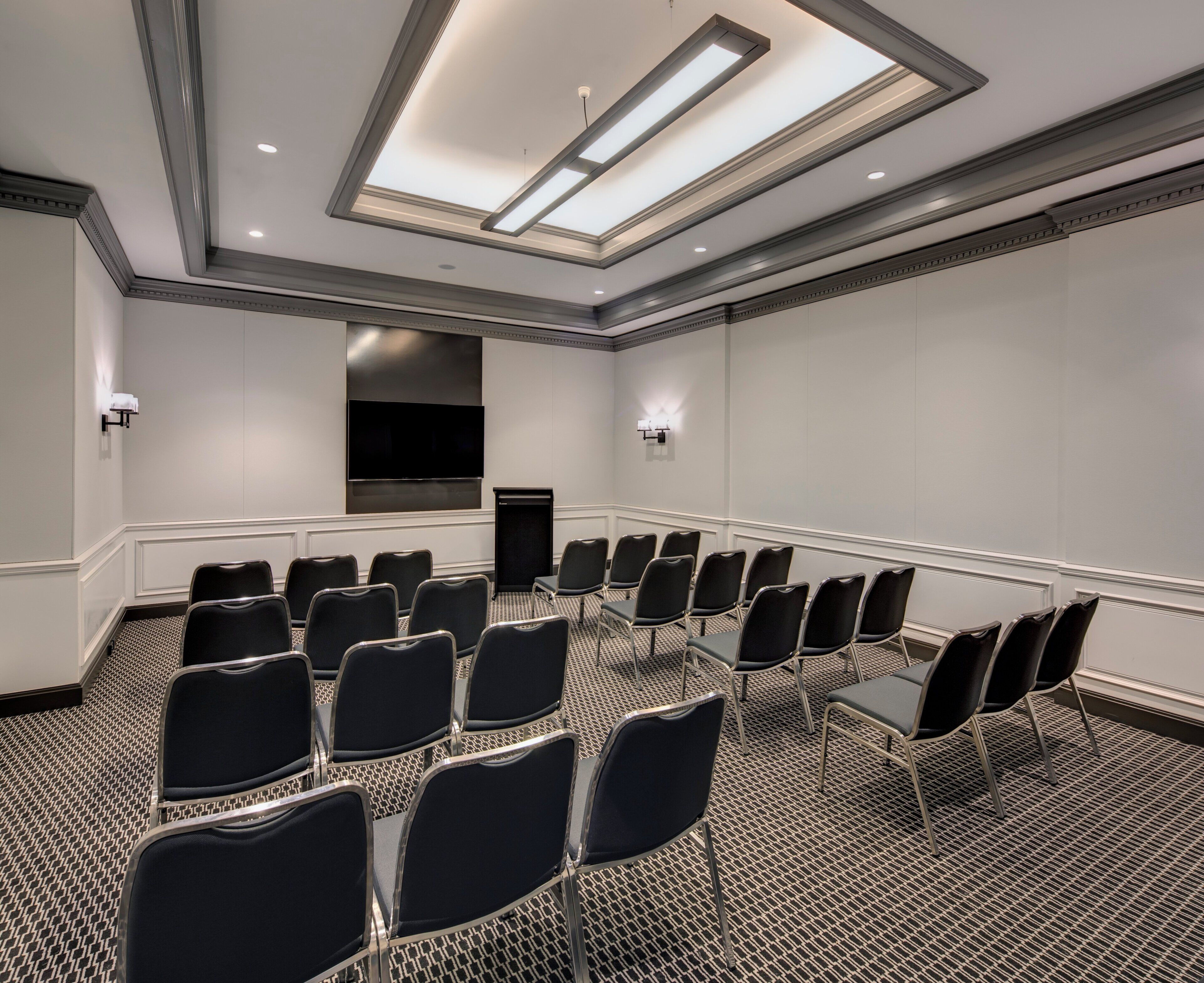A conference room with a long table, rows of chairs, a flat-screen TV, and a ceiling with skylights.