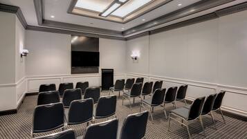 A conference room with a long table, rows of chairs, a flat-screen TV, and a ceiling with skylights.